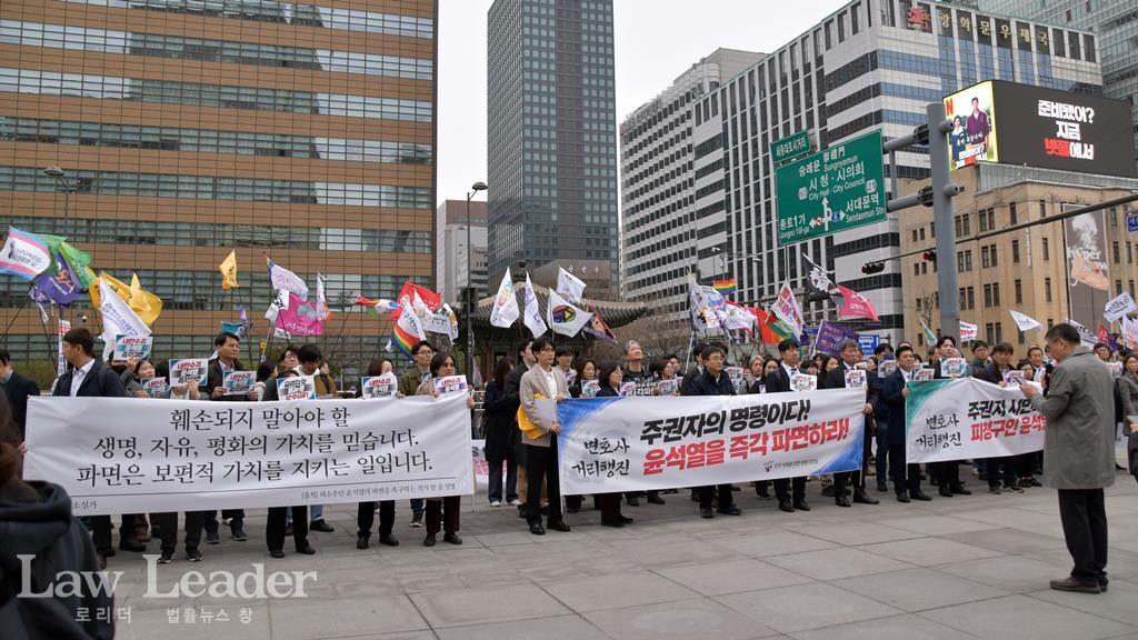 윤석열 즉각 파면 촉구 변호사 거리행진 도중 뒤쪽으로 깃발을 든 시민들이 광화문 북광장으로 행진해 입장하고 있다.