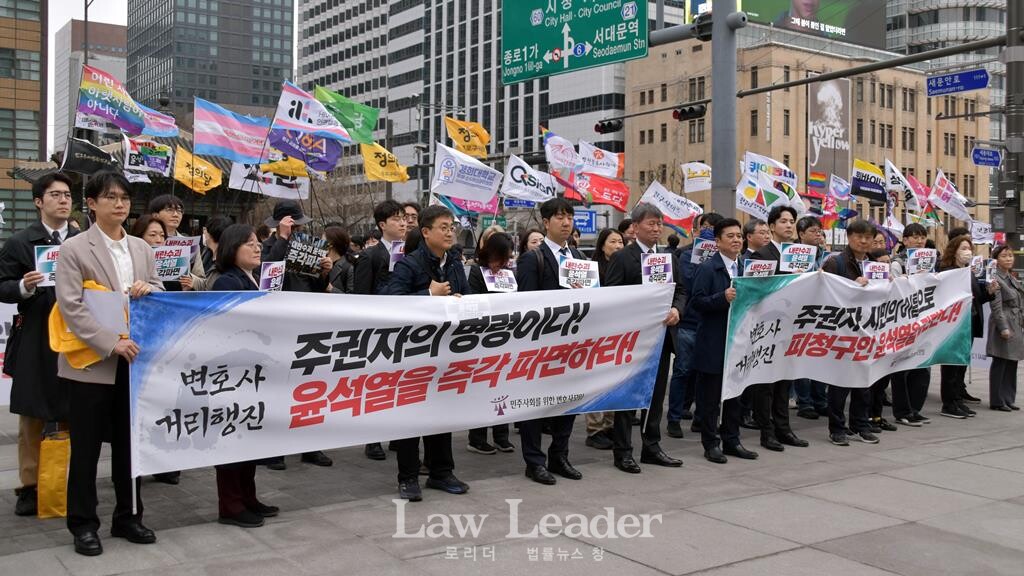 윤석열 즉각 파면 촉구 변호사 거리행진 도중 뒤쪽으로 깃발을 든 시민들이 광화문 북광장으로 행진해 입장하고 있다.
