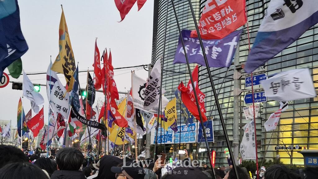 헌법재판소가 위치한 안국동 근처에서 열린 비상행동 집회에서 시민 참가자들과 야당 당원들이 깃발을 흔들며 행진하고 있다.
